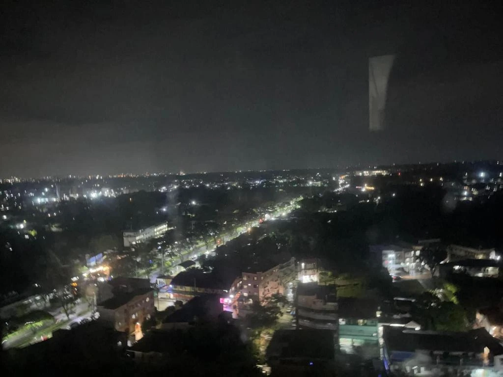 Nighttime aerial view of a city with illuminated streets, buildings, and scattered lights under a dark sky.