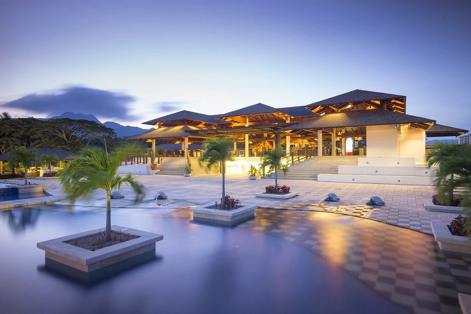 Luxury resort pavilion with swimming pools, palm trees, and mountain views at sunset.