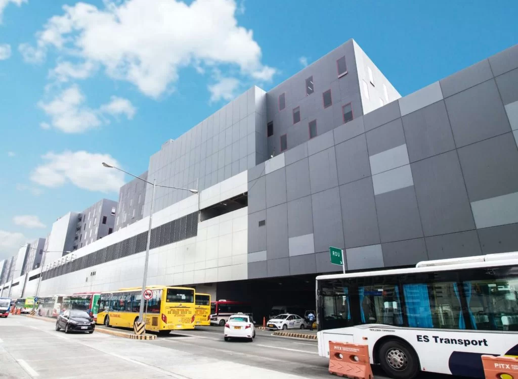 Modern commercial building in Cavite with buses and vehicles along the street under a bright blue sky.