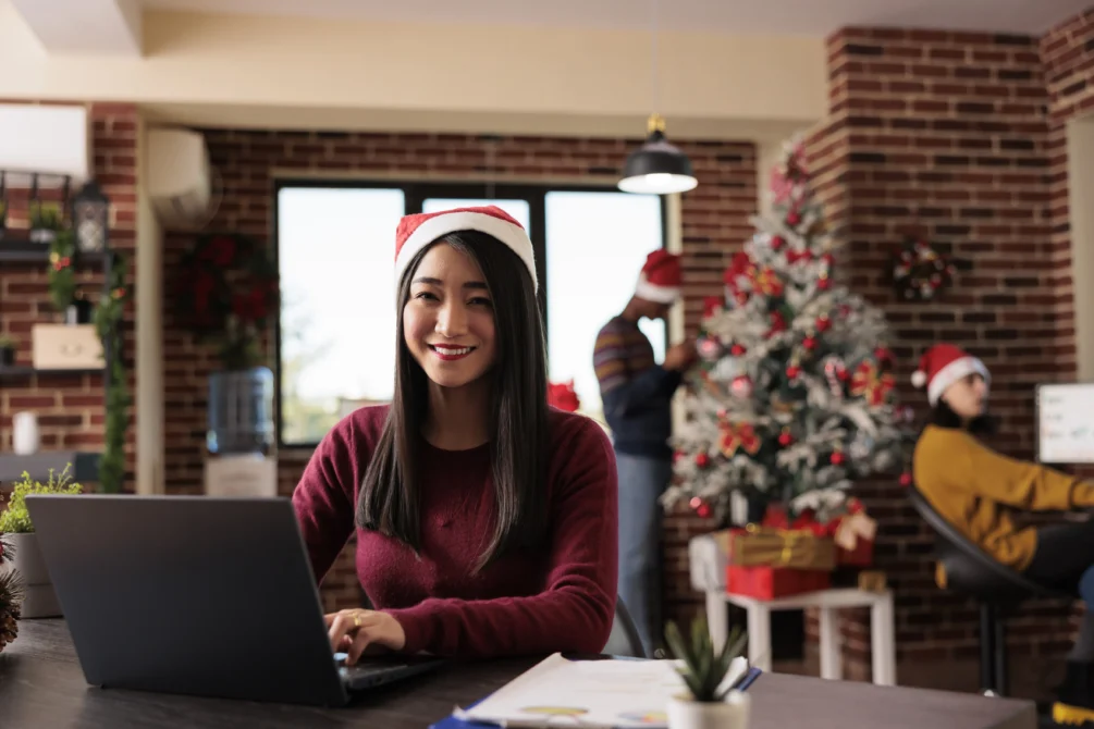 Woman wearing a Santa hat working on a laptop in a festive café