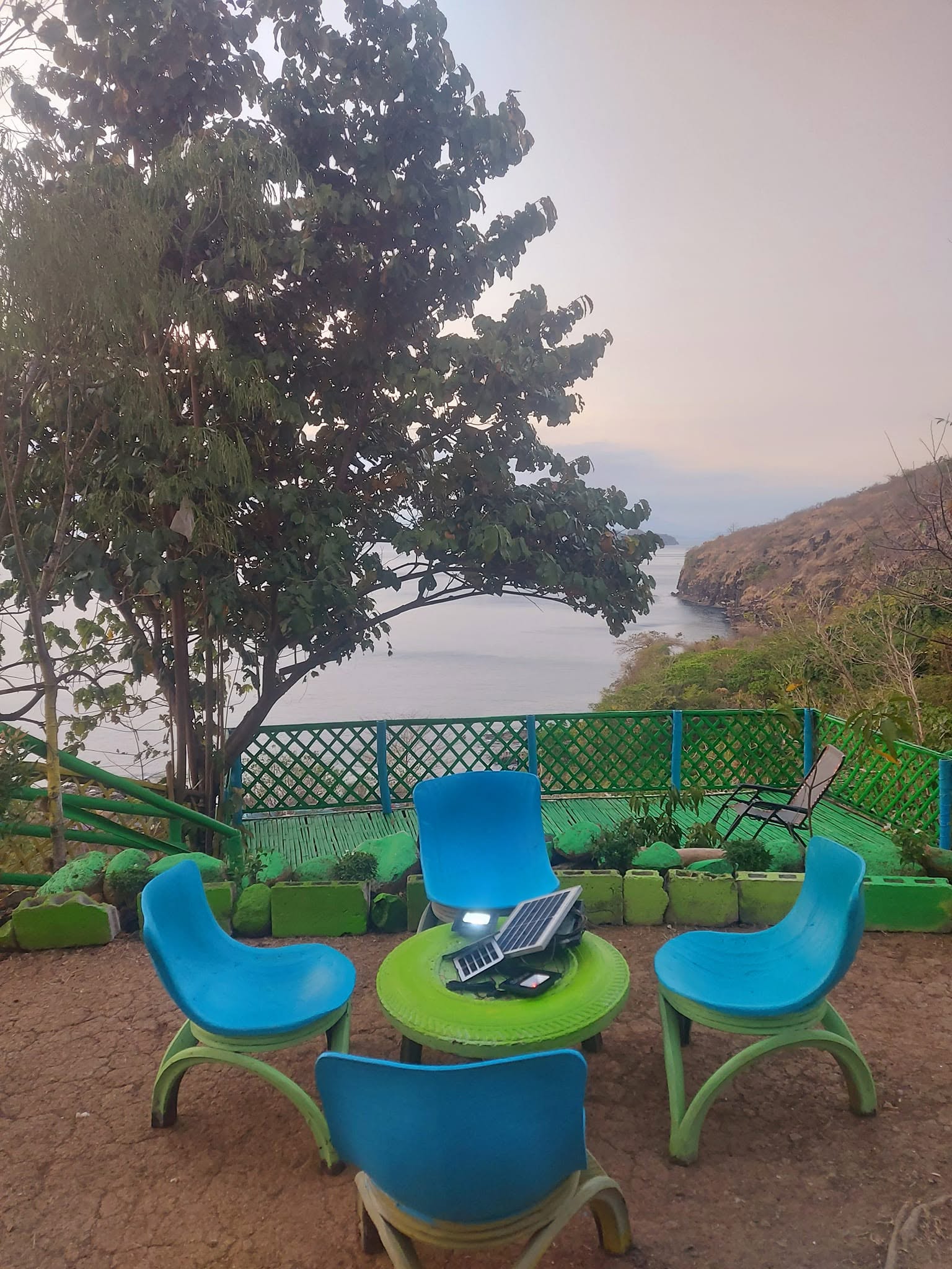 Outdoor seating with blue chairs and a green table at Backpackers' Inn Campsite & Viewdeck, overlooking the sea in Maragondo…