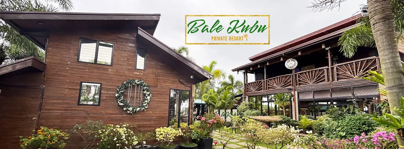 Bale Kubu in Alfonso features rustic wooden buildings surrounded by lush greenery and tropical plants.