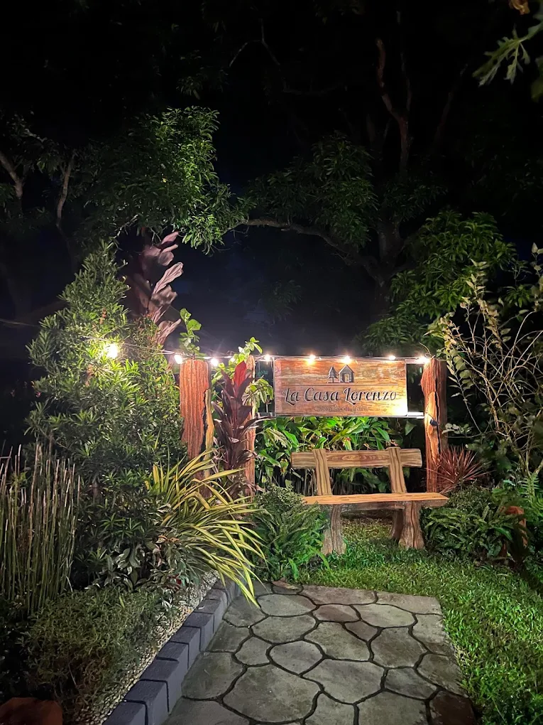 La Casa Lorenzo entrance with wooden bench and lush greenery, warmly lit at night in Alfonso, Cavite.