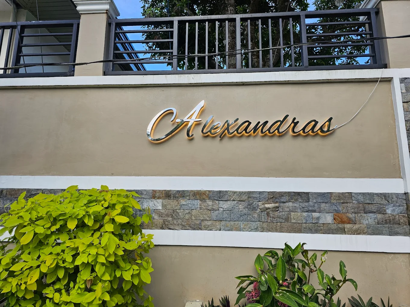 Alexandras Guest House sign on a stone wall with green plants in Alfonso, Cavite.
