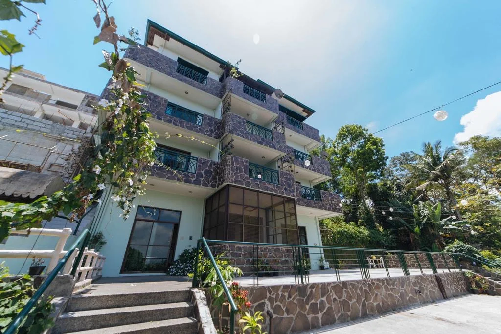 MC Mountain Home Apartelle in Alfonso, featuring a multi-story building with stone facade and lush greenery.