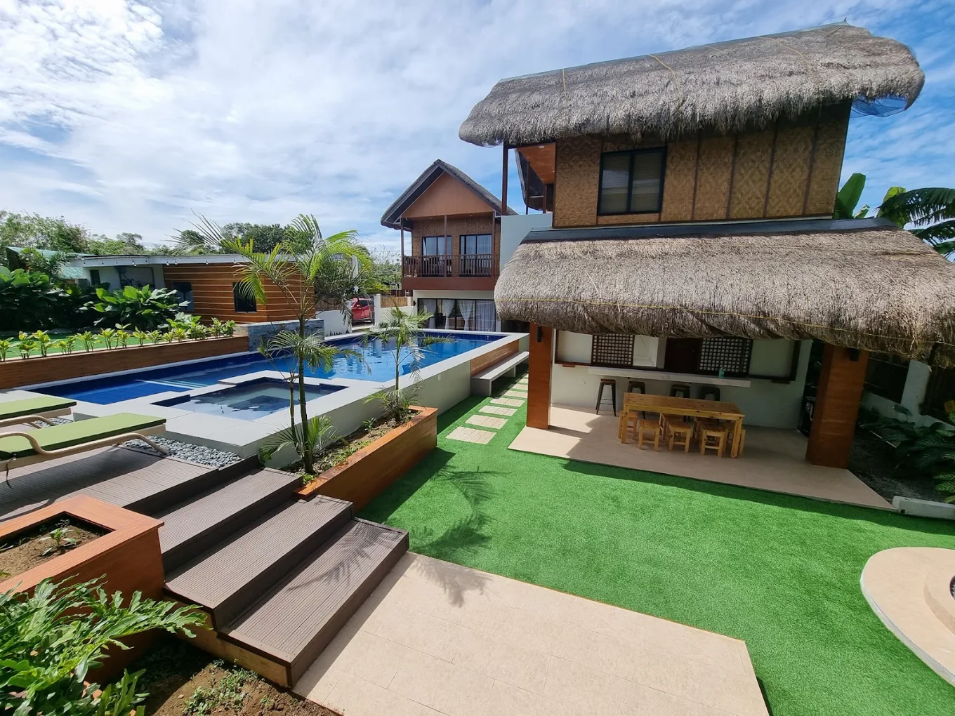 Tropical villa with pool and thatched roof at Casa Cataluna, Alfonso, surrounded by lush greenery and clear skies.