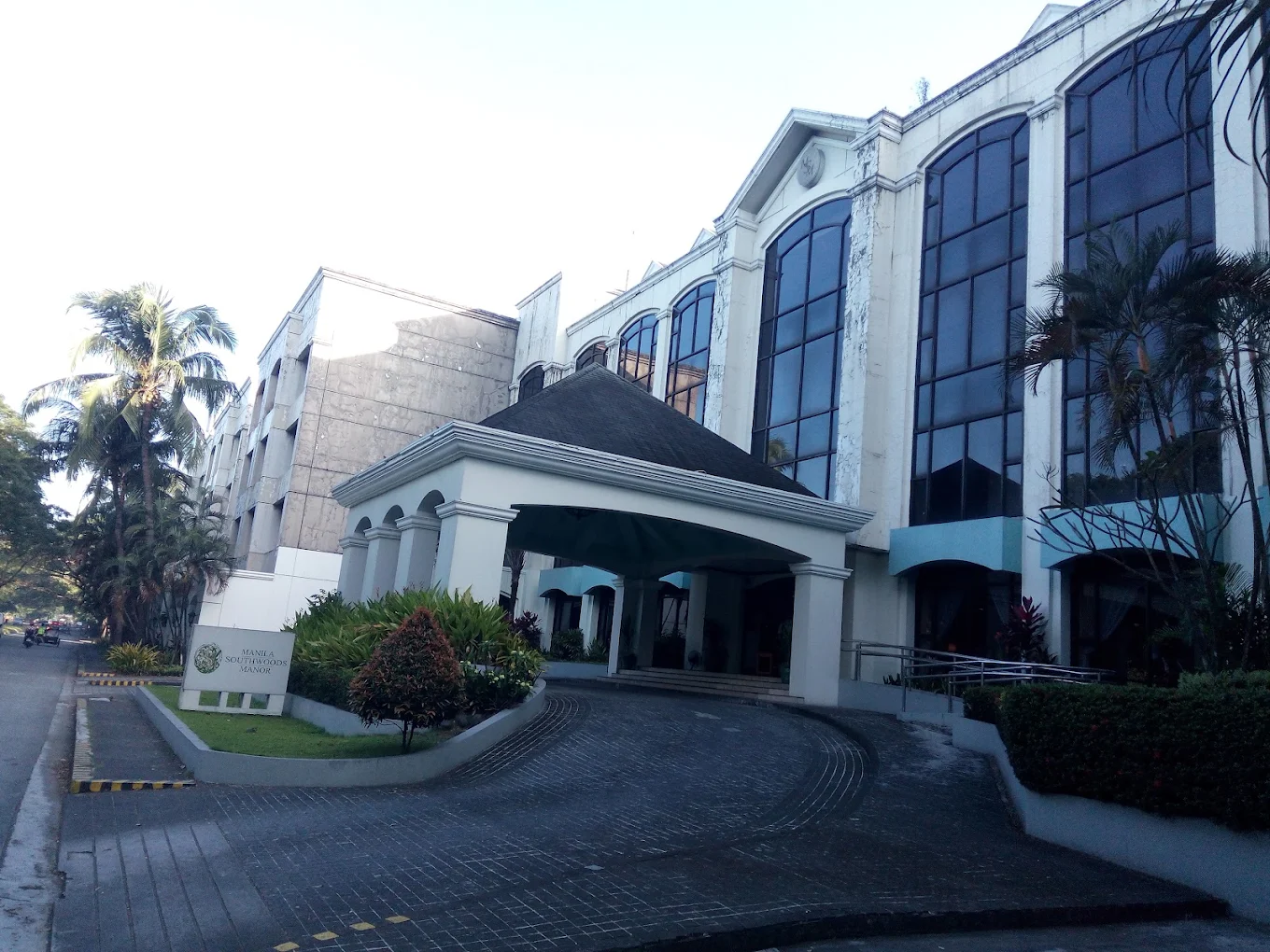 Manila Southwoods Manor entrance with large windows and lush greenery in Carmona, Cavite.
