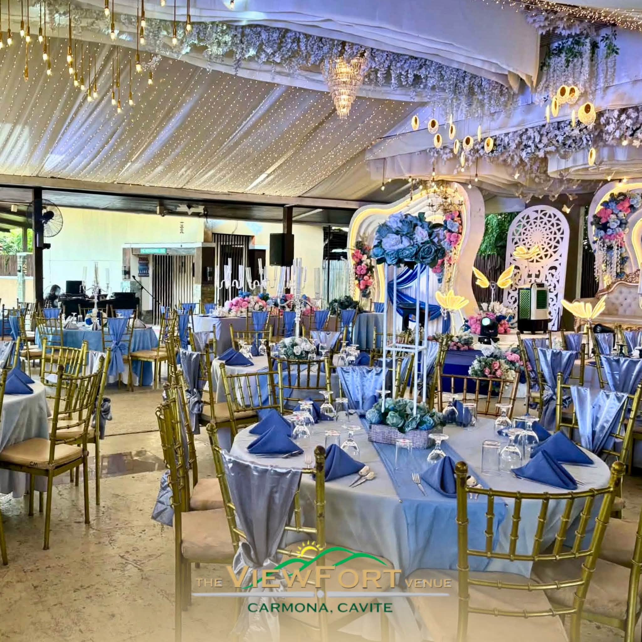 Elegant event setup at The Viewfort Venue in Carmona, featuring blue and gold decor with floral centerpieces.