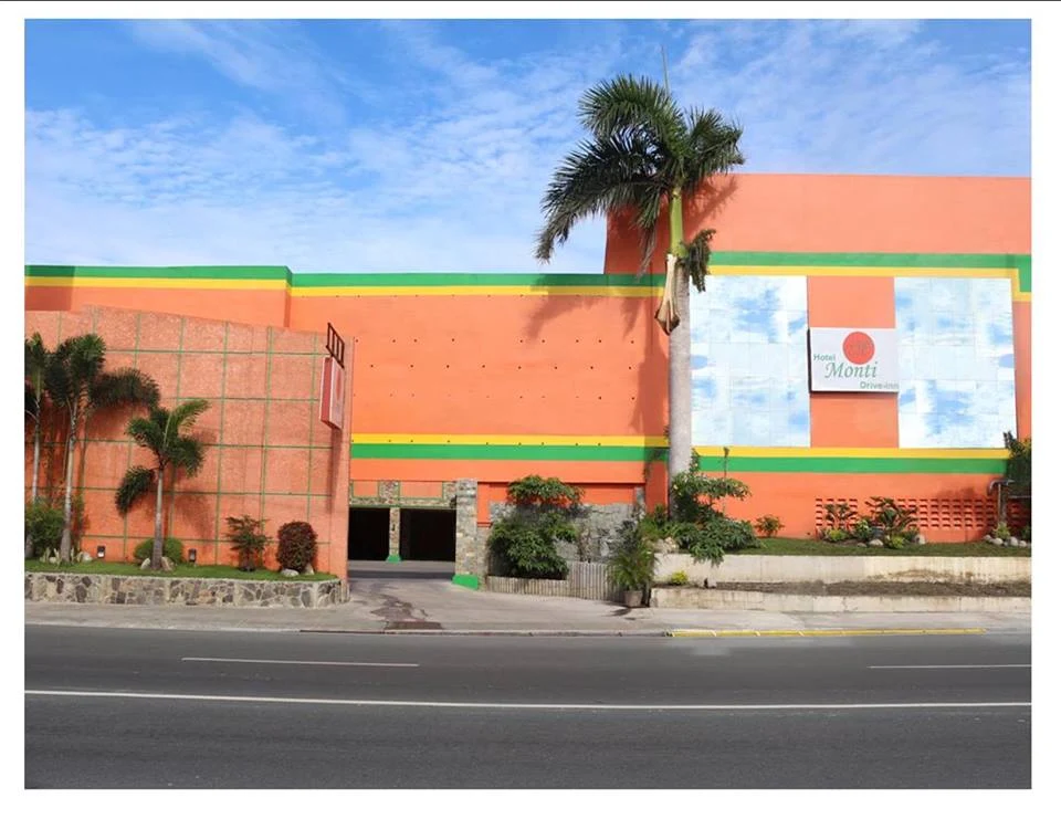 Hotel Monti Drive Inn in Carmona with vibrant orange facade, palm trees, and clear blue sky.