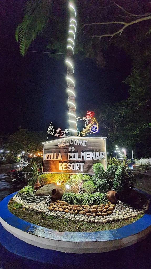 Welcome sign at Villa Colmenar Natural Spring Resort, Indang, surrounded by plants and decorative lights at night.
