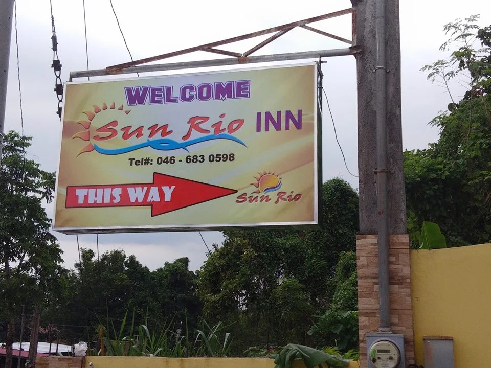 Sun Rio Apartelle sign with contact info and arrow, surrounded by trees in Trece Martires.