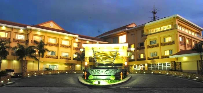 Tanza Oasis Hotel and Resort entrance with illuminated signage and surrounding palm trees at dusk in Tanza, Cavite.