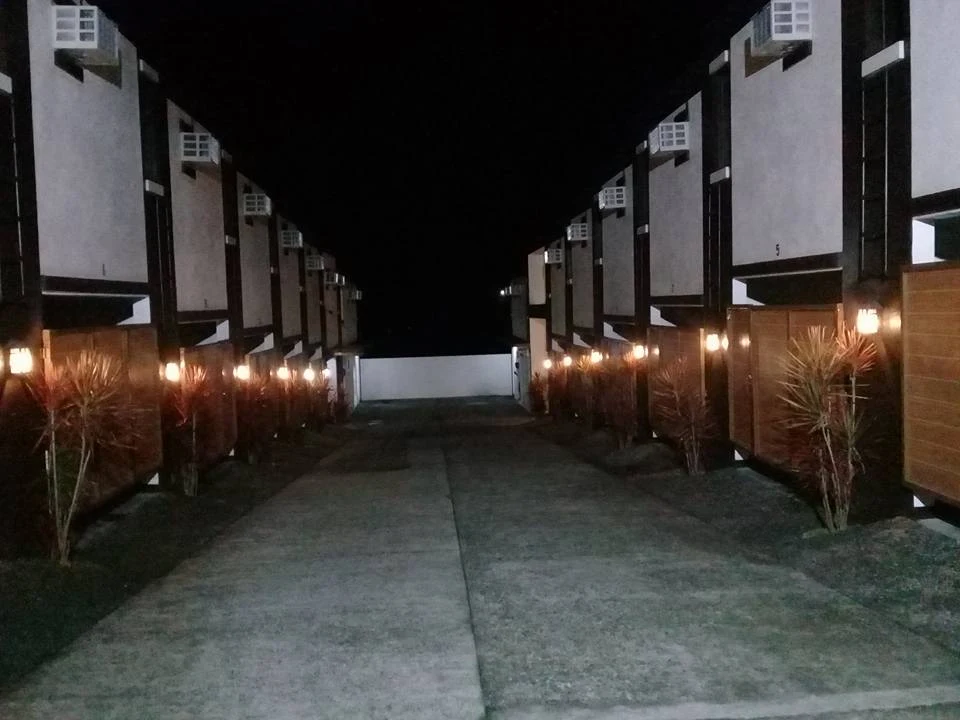 Night view of Sweet-Country Inn in Silang, featuring a well-lit pathway lined with modern buildings and plants.
