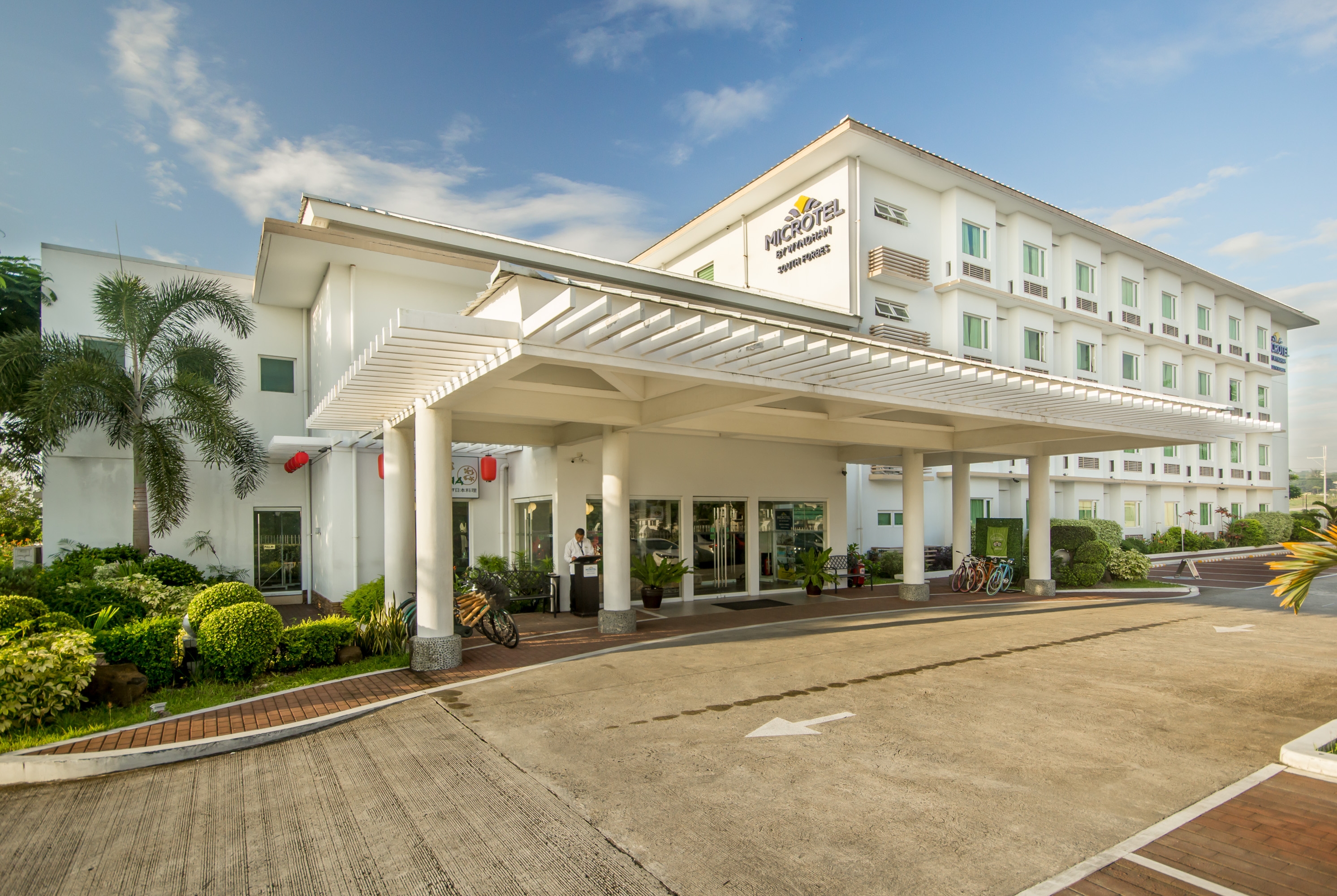 Microtel by Wyndham South Forbes entrance with landscaped greenery and a clear blue sky in Silang, Cavite.