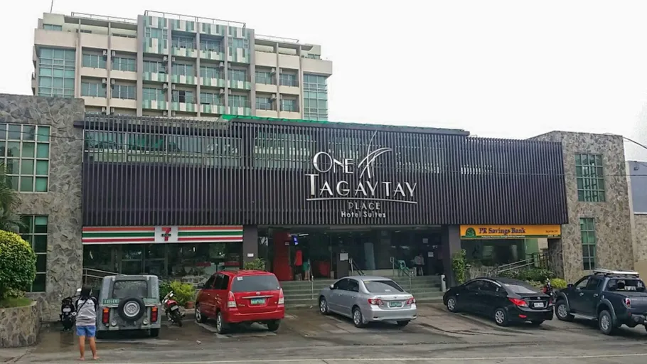 One Tagaytay Place Hotel Suites facade with parked cars, 7-Eleven, and PR Savings Bank in Tagaytay.