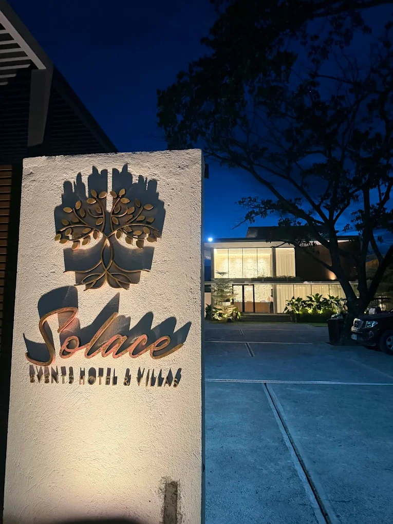Solace Events Hotel & Villas entrance sign illuminated at night, General Trias, with building and trees in the background.