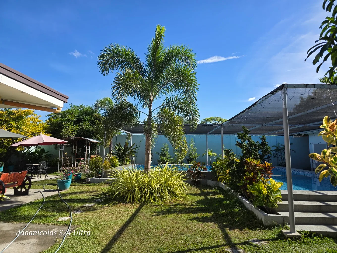 Lush garden and pool area at Rilie's Private Resort, General Trias, with palm trees and vibrant plants under a clear sky.