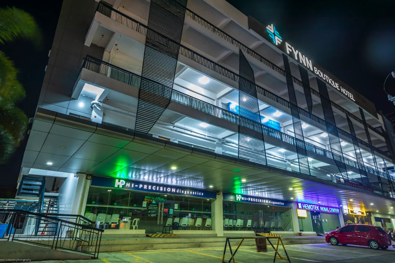 Fynn Boutique Hotel in Bacoor at night, showcasing modern architecture with illuminated signage and nearby businesses.