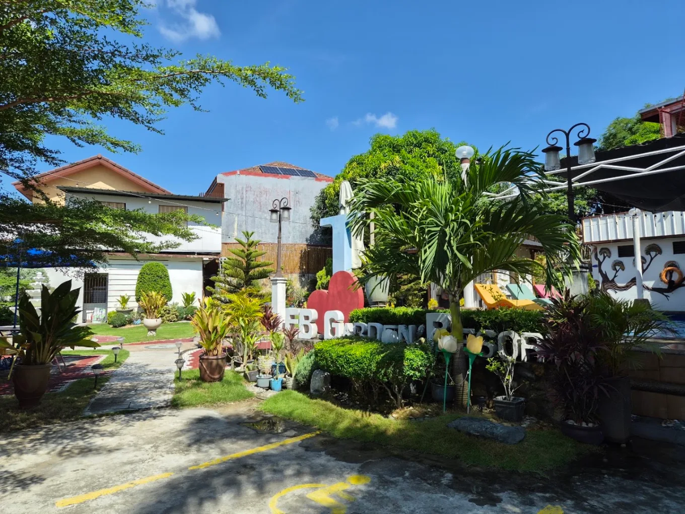Lush garden with palm trees and signage at EB Garden Resort and Venue, Bacoor, under a clear blue sky.