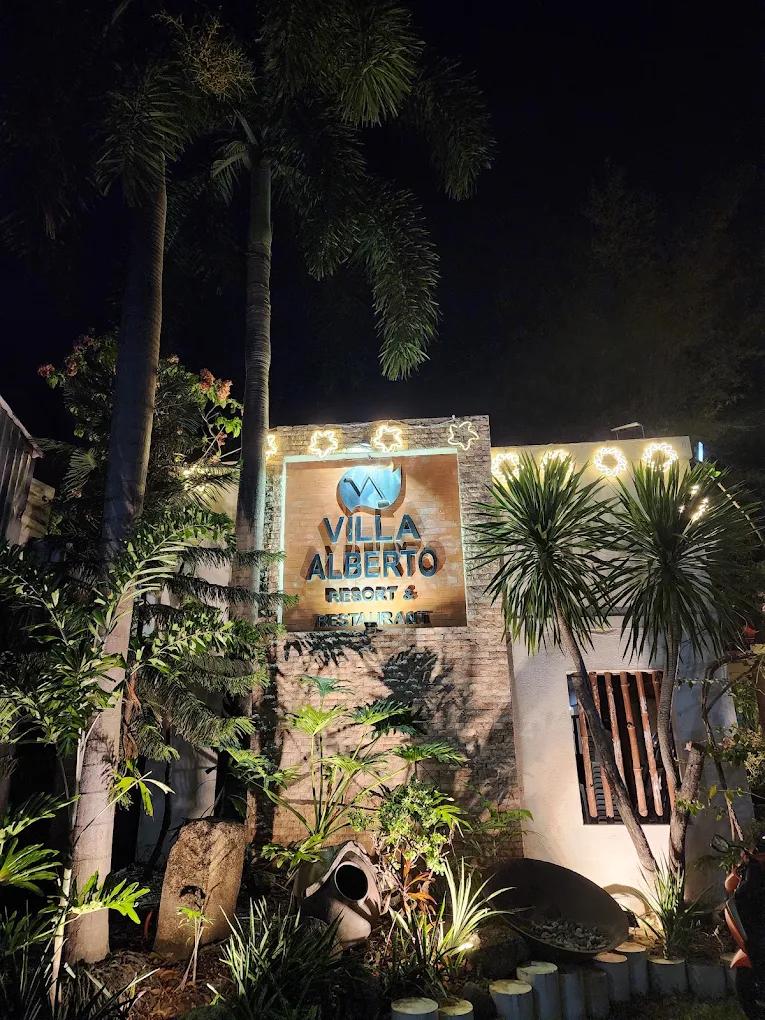 Villa Alberto Resort entrance sign illuminated at night, surrounded by lush tropical plants in Bacoor, Cavite.