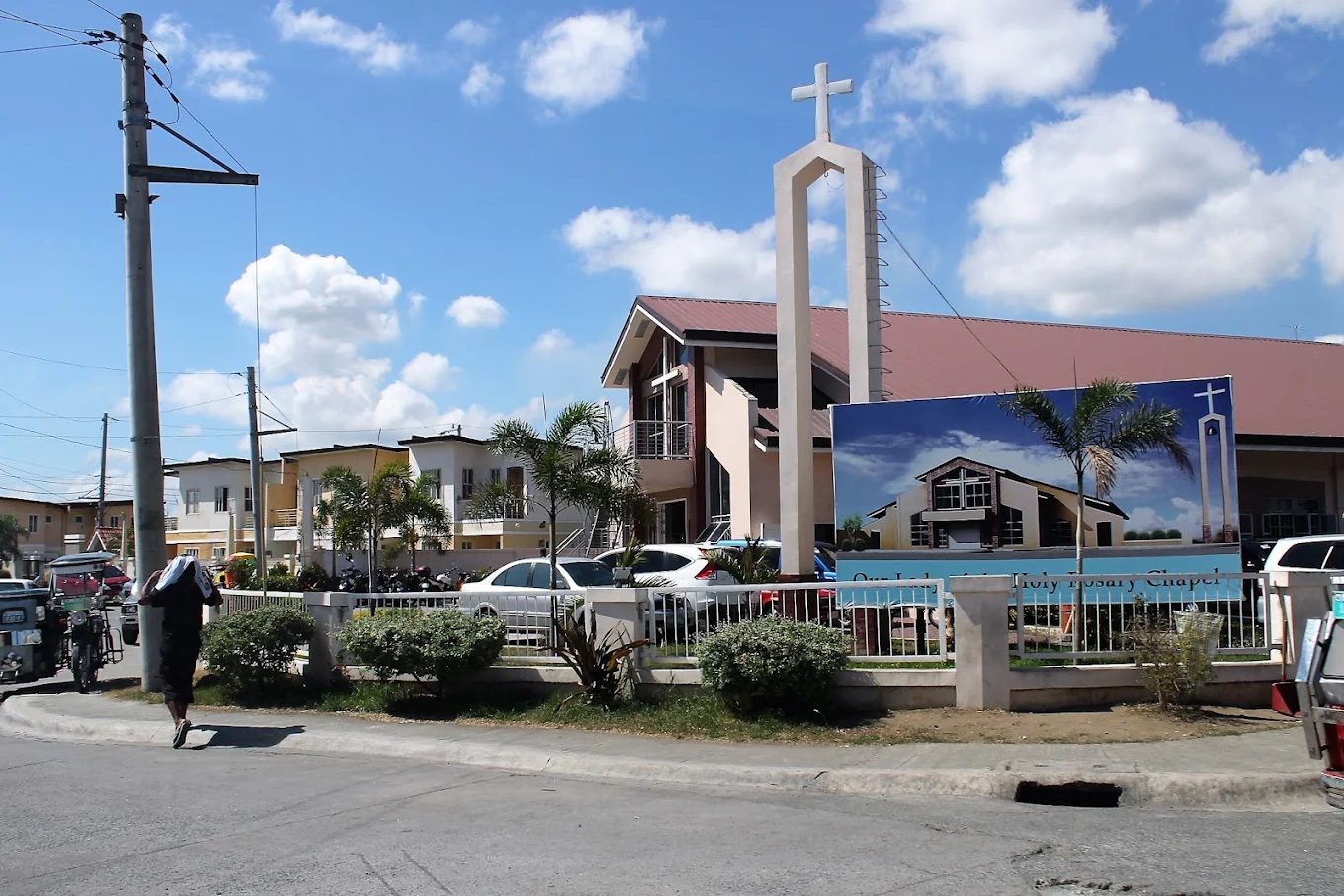Nuestra Señora del Santissimo Rosario Parish in Carmona with a tall cross and surrounding greenery under a blue sky.